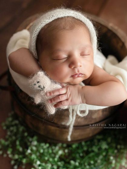 Pure innocence. This newborn, wearing a simple bonnet and holding a tiny teddy bear, looks so peaceful resting in a rustic bucket.