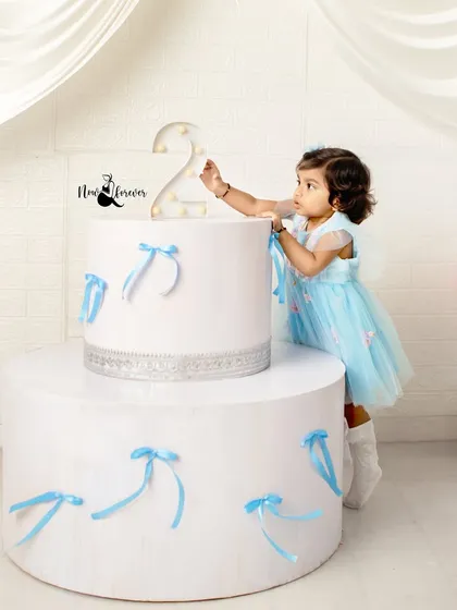 This little princess is celebrating her second birthday in a beautiful blue dress. The elegant, oversized cake prop creates a magical setting.