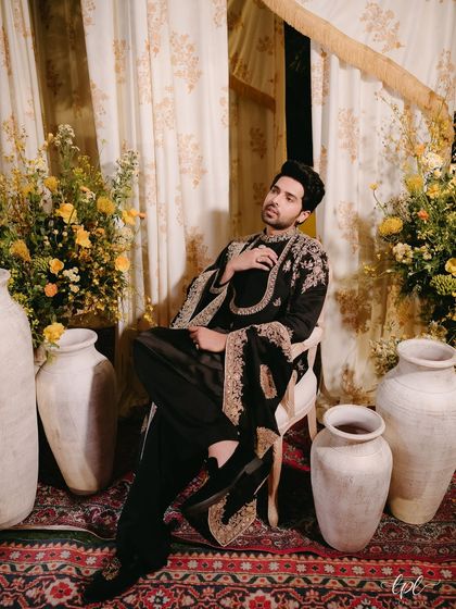 A portrait of the groom at the Mehfil, seated amidst large earthen pots and arrangements of yellow flowers that complemented his black and gold attire.