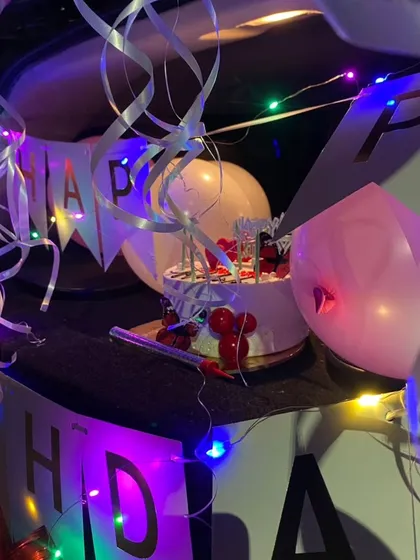 This shot focuses on the details of the car trunk decor, with swirling ribbons, a birthday cake, and a banner illuminated by multi-colored fairy lights for a festive feel.