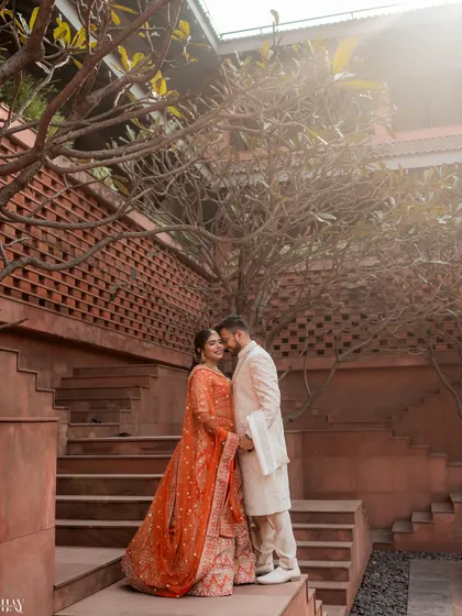 A romantic portrait on the terracotta steps of the resort. The warm tones of the architecture complement the bride's orange lehenga, and the surrounding trees frame the couple beautifully.