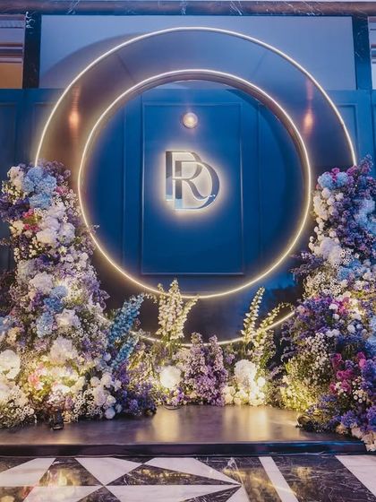 A beautiful photo-op corner at the Sangeet, with a neon-lit monogram and lush floral arrangements in shades of blue and purple.