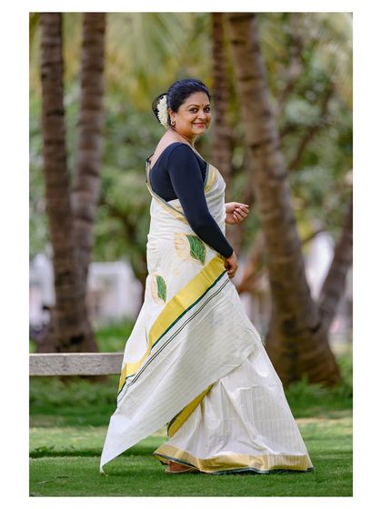 A beautiful outdoor shot for a Kerala Onam saree. The natural lighting and green background complement the traditional white and gold of the attire.