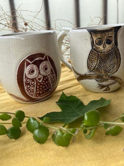 A pair of owl mugs, each with a unique hand-drawn design. They are ready to find a new home.