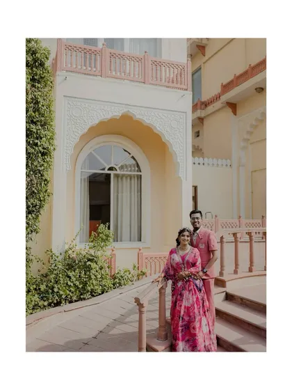 A beautiful portrait of the couple at their Jaipur destination wedding. The bride's floral gown and the groom's pink shirt perfectly complement the romantic setting.