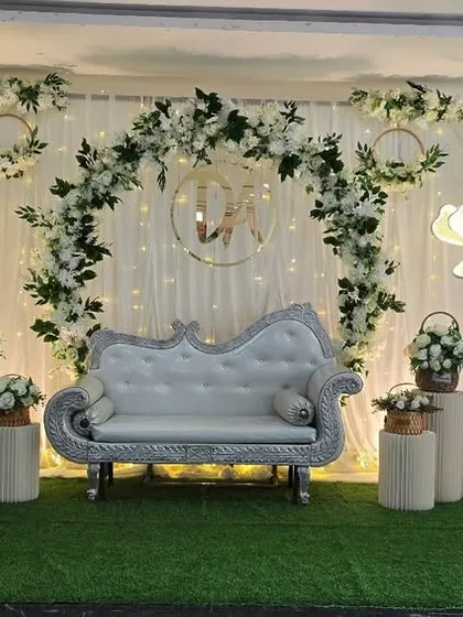 A classic wedding reception stage with a white floral arch, a custom monogram, and a silver diwan, creating a timeless and romantic setting.