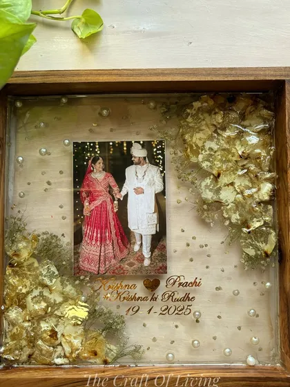 This wooden frame features preserved white and gold flowers, creating a very regal and elegant look. The couple's photo is placed centrally, with their names and wedding date below.