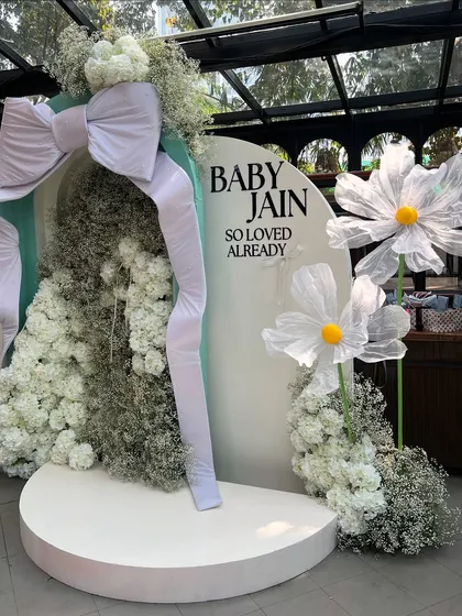 For this dreamy baby shower, we created a bespoke backdrop featuring a giant fabric bow, clouds of baby's breath, and oversized whimsical daisies. This is our signature modern and chic event styling.