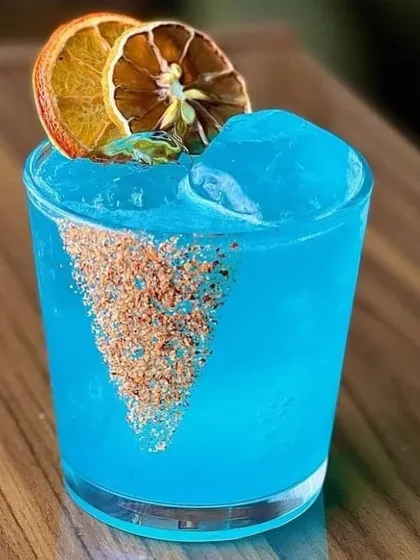 This striking Blue Lagoon mocktail is a visual delight. Garnished with dehydrated orange slices and a spiced rim, it's a popular choice for guests who love a vibrant and tropical drink.