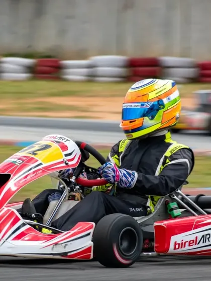 Driver Hunner Singh, identifiable by his brightly colored helmet, expertly maneuvers his Birel ART kart through a pack of competitors.