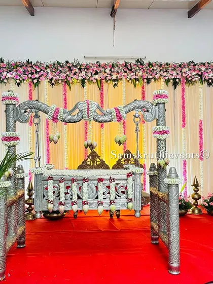 A grand silver cradle setup for a naming ceremony. The backdrop of hanging floral strings and a lush flower canopy creates a luxurious and celebratory atmosphere for this special occasion.