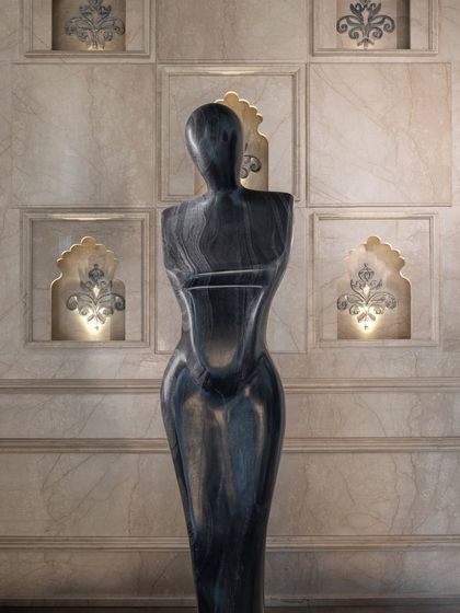 A closer view of the sculpture reveals the beautiful striations in the black marble. It stands against a backdrop of custom wall niches with traditional jharokha-inspired arches, blending modern art with heritage details.
