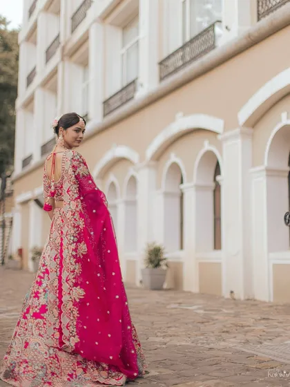 A bride looks back over her shoulder, showing off the beautiful back of her gown and the vibrant pink dupatta.