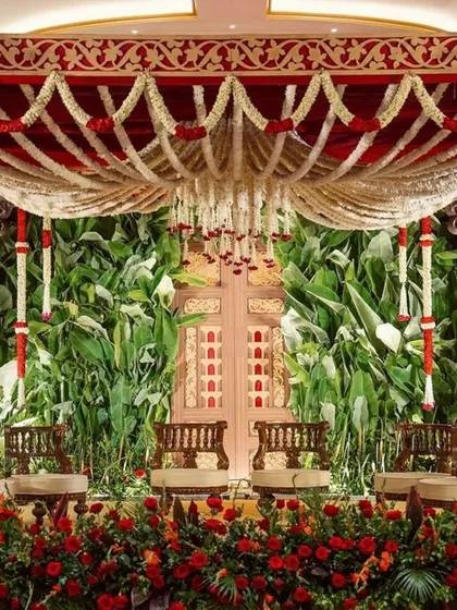 A truly magnificent South Indian wedding mandap that honors tradition with its grandeur. The lush green backdrop contrasts beautifully with the rich red and white floral garlands, creating a sacred and visually stunning space for the ceremony.