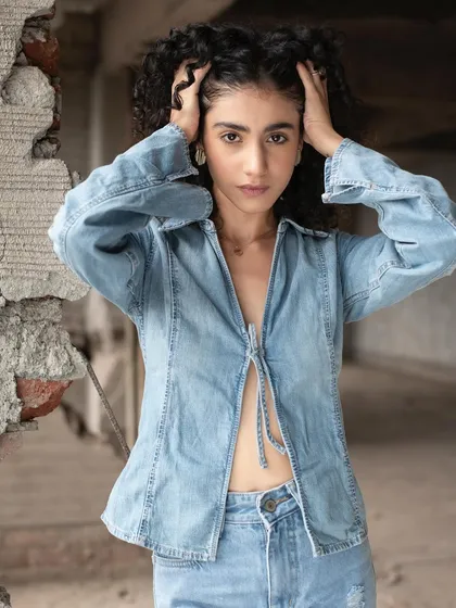 A model with beautiful natural curls in an industrial setting. The makeup is minimal and subtle, enhancing her features without distracting from her striking hair and expression.