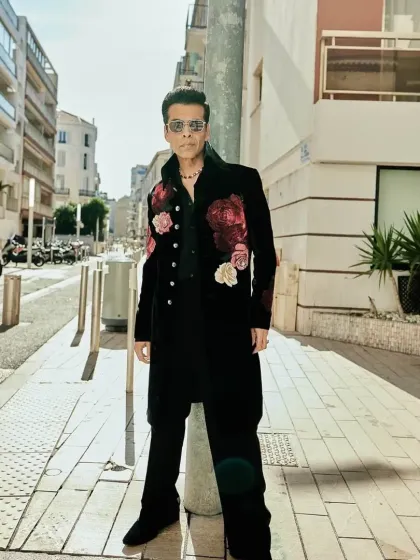 Karan Johar wearing a custom black longline jacket with bold, hand-embroidered floral motifs in shades of red and pink. This Indowestern piece is crafted from rich velvet for a truly luxurious feel.