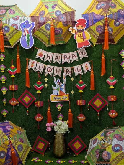 This Lohri backdrop uses a green grass wall as a base, decorated with a "Happy Lohri" banner, colorful kites, and traditional embroidered umbrellas.