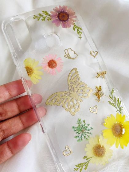 This resin phone case is extra special, with a delicate butterfly charm embedded among the pressed flowers. It's a perfect example of how we can personalize your accessories.