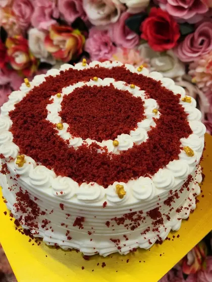 A beautifully decorated Red Velvet cake. This design features a spiral of red velvet crumbs and delicate white frosting, finished with a sprinkle of golden pearls for an elegant touch.