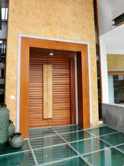 The entrance to this home makes a statement with a massive wooden door and a unique glass floor over a water feature. This design choice immediately establishes a connection with nature and a sense of modern luxury.