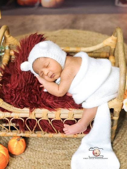 A cozy and rustic scene for a sleeping newborn. Dressed in a white bear bonnet, the baby is nestled in a miniature wooden bed, surrounded by warm candlelight and autumnal props for a storybook feel.
