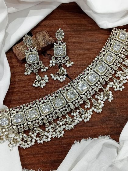 A popular choker design featuring square-cut stones, available in a variety of colors like emerald green, white, aqua blue, and baby pink. The matching earrings complete this elegant and modern ethnic set.