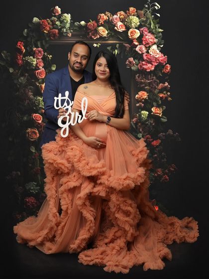 A joyful gender reveal moment. This couple celebrates the news that "it's a girl" while surrounded by a floral frame and dressed in a beautiful peach gown.