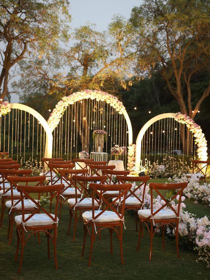 A beautiful ceremony setup for an outdoor wedding. Three floral arches are adorned with white flowers and hanging light bulbs, creating a romantic backdrop for the vows.