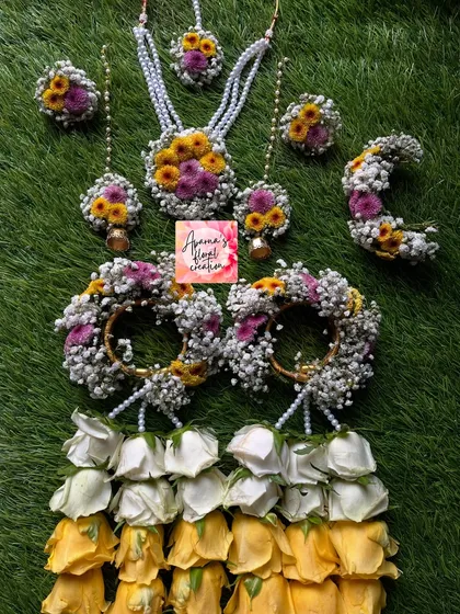 A full view of the multi-colored Haldi set. It includes a necklace, earrings, maang tikka, and haath phool with kalire made from white, yellow, and pink roses.