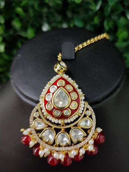 A bold and beautiful maang tikka with red enamel work and large kundan stones, designed to be the centerpiece of your look.