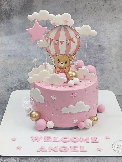 A sweet "Welcome Angel" cake. This pink cake features a teddy bear in a hot air balloon, surrounded by fluffy clouds and stars.