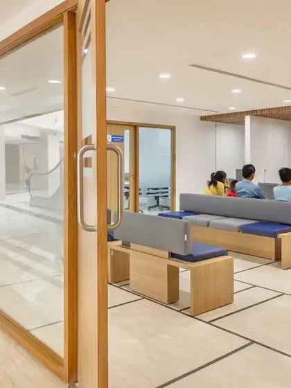 The admissions area is designed with semi-private seating arrangements to offer comfort and discretion for patients and families during the registration process. The use of wood and soft upholstery creates a less clinical, more reassuring environment.