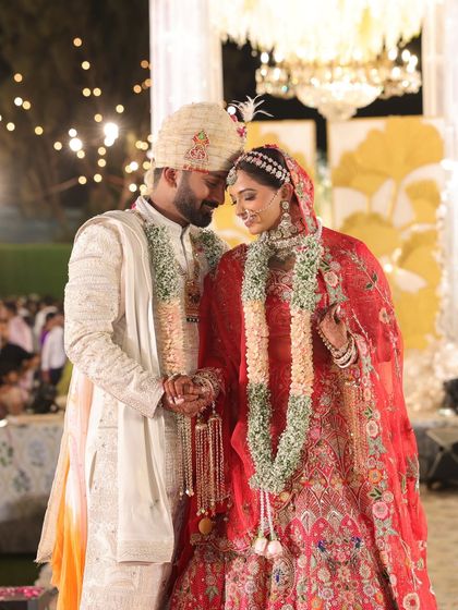 A full-length shot of the bride and groom during their varmala ceremony. This image captures the grandeur of the moment, with the couple standing on a beautifully decorated stage.