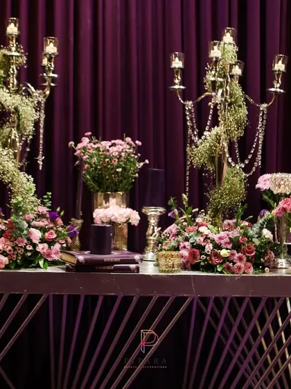 A modern console table dressed in florals and candelabras. The geometric base of the table contrasts with the organic shapes of the flowers and the classic candelabras, creating a dynamic look.