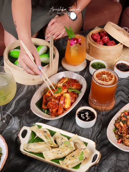A lively table scene at a Pan-Asian restaurant, with a hand reaching for dumplings. This image captures the dynamic atmosphere of a shared meal with friends.