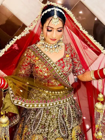 A beautiful shot of a bride in her olive and red lehenga, holding her veil. The soft lighting and her pose create a classic and timeless bridal portrait.
