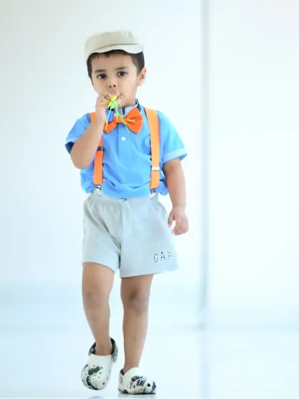 A stylish little boy dressed like Blippi, walking confidently in a bright, open corridor.