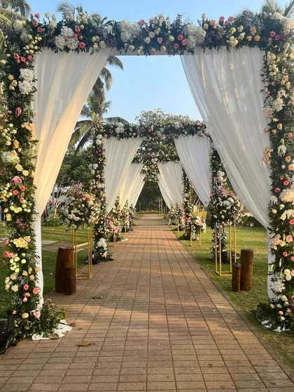 We design elegant pathways that lead to beautiful beginnings. This stunning wedding aisle features a series of floral arches and sheer white drapes, creating a dreamy and romantic walkway for a garden ceremony.