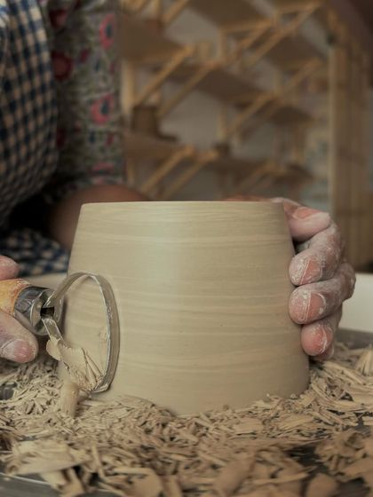 A close up of a trimming tool carving away clay from the base of a pot. This process requires a steady hand and a good eye to create a clean, even finish.