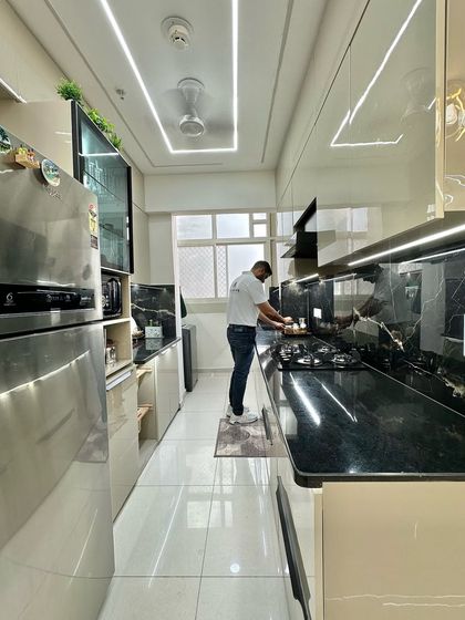 Final touches on a beautiful modular kitchen. The design features beige high-gloss cabinets, a black marble countertop and backsplash, and a large side-by-side refrigerator.