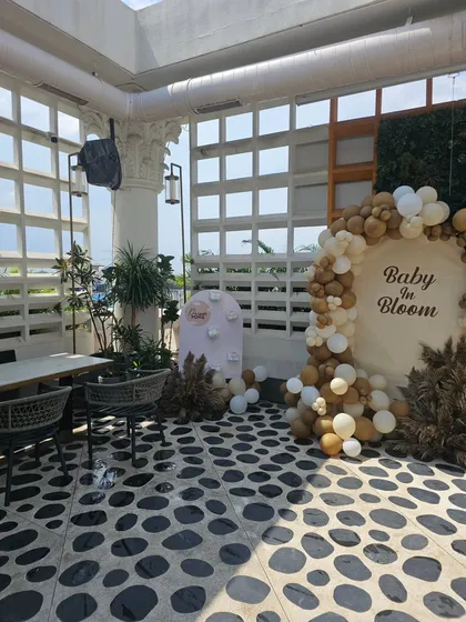 A wide view of the "Baby in Bloom" baby shower setup on a terrace. The natural light highlights the neutral-toned balloon arch and rustic decor elements.