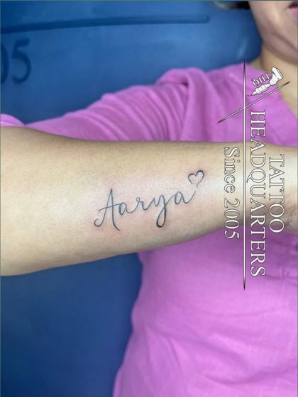 The name "Aarya" in a lovely cursive font with a heart outline at the end, inked on the forearm.
