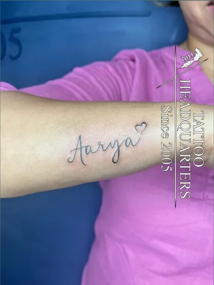 The name "Aarya" in a lovely cursive font with a heart outline at the end, inked on the forearm.