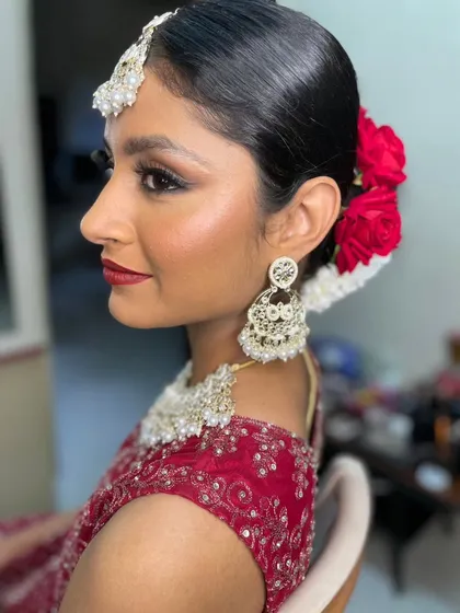 This is for the bride who loves a touch of drama. We went for a glamorous reception look with a sharp winged eyeliner, a bold red lip, and radiant, glowing skin. The sleek hair, adorned with vibrant red roses, pulls the entire look together, making it perfect for an evening of celebration.