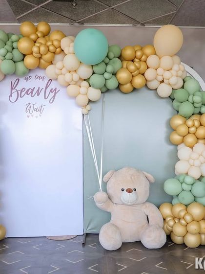 A soft and elegant teddy bear theme using a palette of sage green, beige, and gold. This photo booth setup includes a 'We Can Bearly Wait' sign and interactive boards for guests to guess the baby's gender.