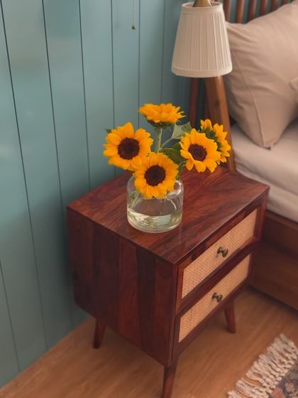 A close-up of the sunflower arrangement on the mid-century modern side table, adding a burst of natural color against the calming blue wall.