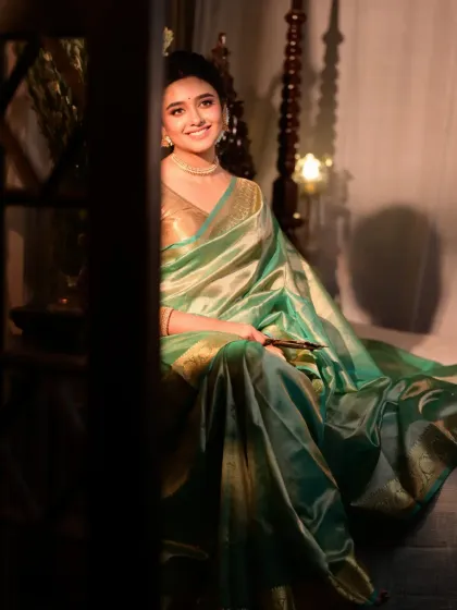 A candid shot of a model in a light green saree, sitting on a traditional swing. The play of shadow and light from the side creates a mysterious and alluring mood.
