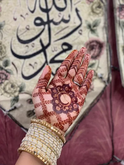 This Eid design features a central mandala with a crescent moon, a symbol of the celebration. The surrounding 'jaal' or net pattern and detailed fingertips complete this festive look, which has a beautiful dark stain.