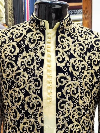 A close-up of a black velvet Jodhpuri jacket, showcasing the dense and luxurious gold embroidery in a swirling pattern. This is a statement piece for any groom.