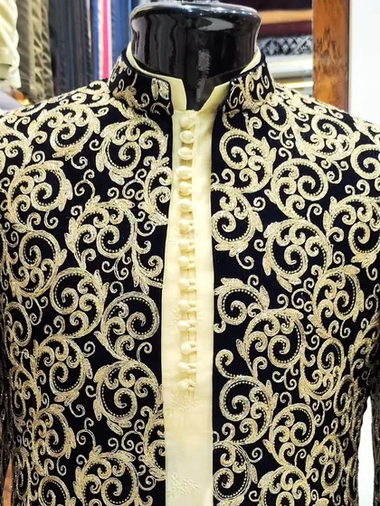 This black velvet sherwani showcases elegance with its intricate gold embroidery. The detailed craftsmanship on the collar and placket makes it a majestic choice for a groom's wedding attire.